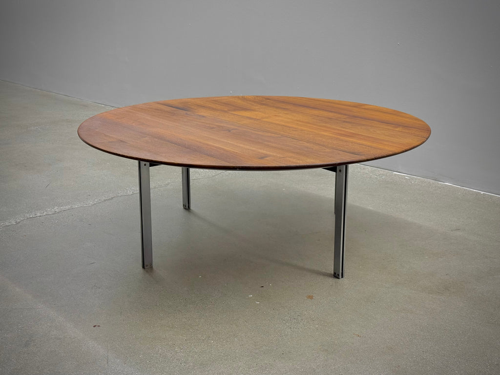 Wooden round table with metal legs on a concrete floor against a gray wall