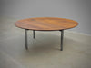 Wooden round table with metal legs on a concrete floor against a gray wall