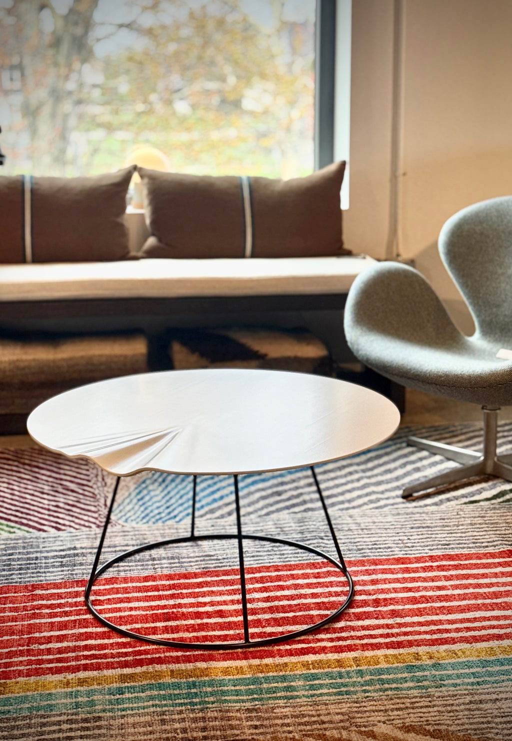 Modern coffee table with a chair on a colorful striped rug in a room with a window.