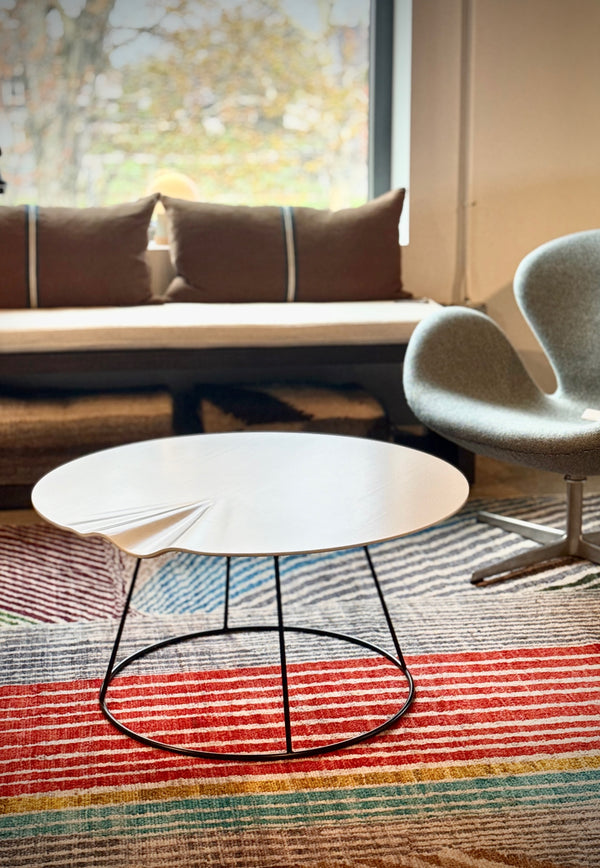 Modern coffee table with a chair on a colorful striped rug in a room with a window.