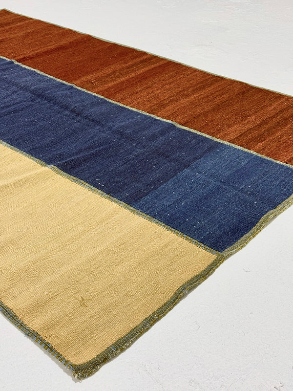 Color-blocked rug with brown, blue, and beige sections on a white background