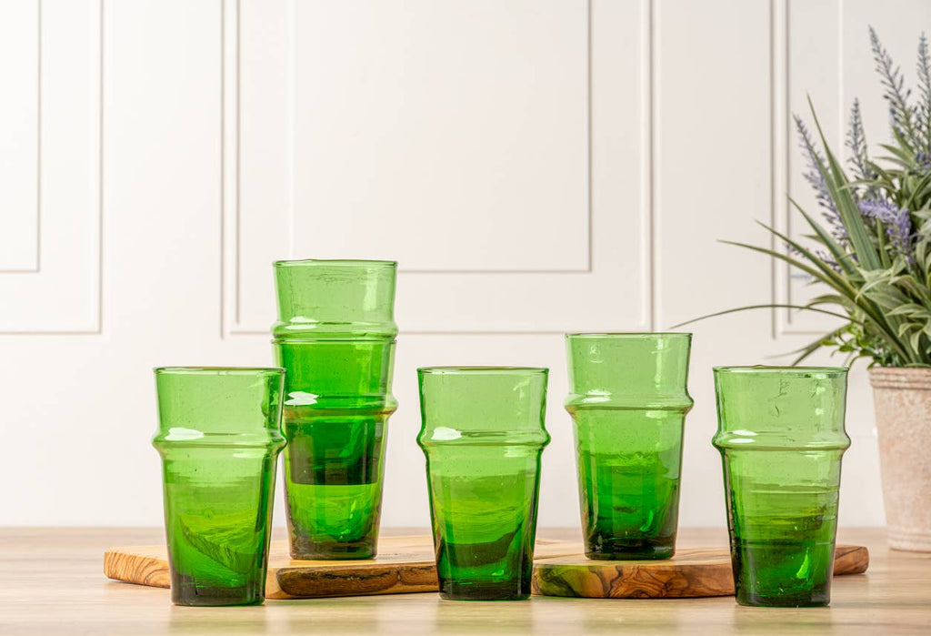 Set of green tumblers on a wooden cutting board with a white cabinet and plant in the background