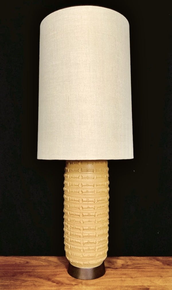 Tall lamp with textured beige base and white shade on a dark background