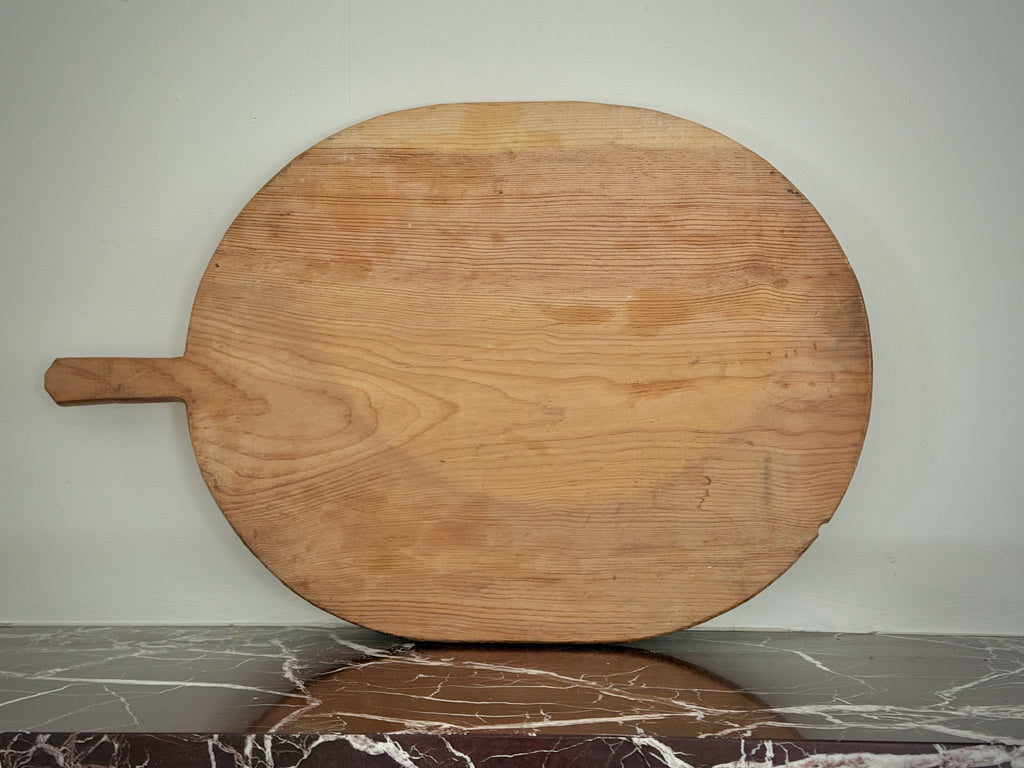 Large wooden pizza peel on a marble floor with a neutral wall background