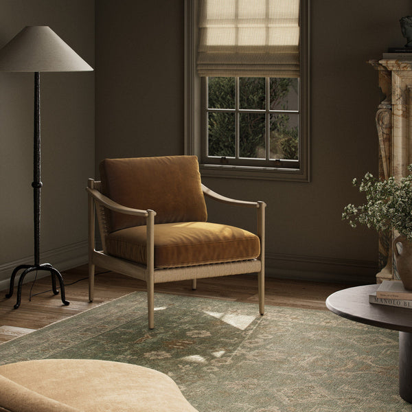 Brown armchair with upholstered cushions in a room with a window, lamp, and rug.