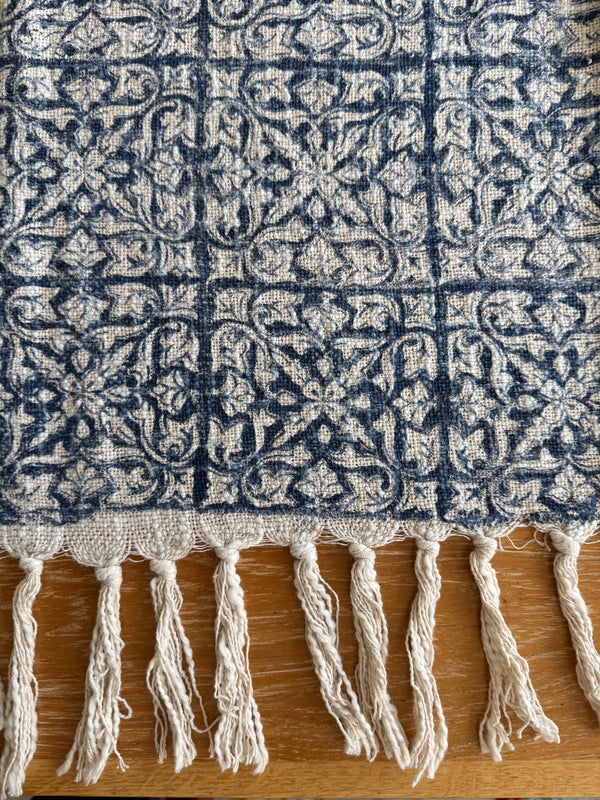 Close-up of a patterned blanket with tassels on a wooden surface
