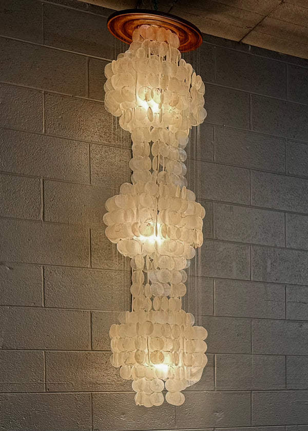Decorative chandelier hanging from a ceiling against a brick wall.