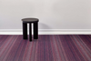 Black stool on a striped purple and red carpet with a white wall background