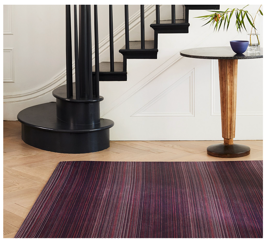 Staircase with black railings and a round wooden table in a room with a purple rug.