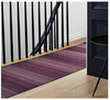 Purple braided rug on a wooden floor in front of a black door and staircase.