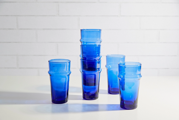 Set of blue glass cups stacked on a white surface with a tiled wall background
