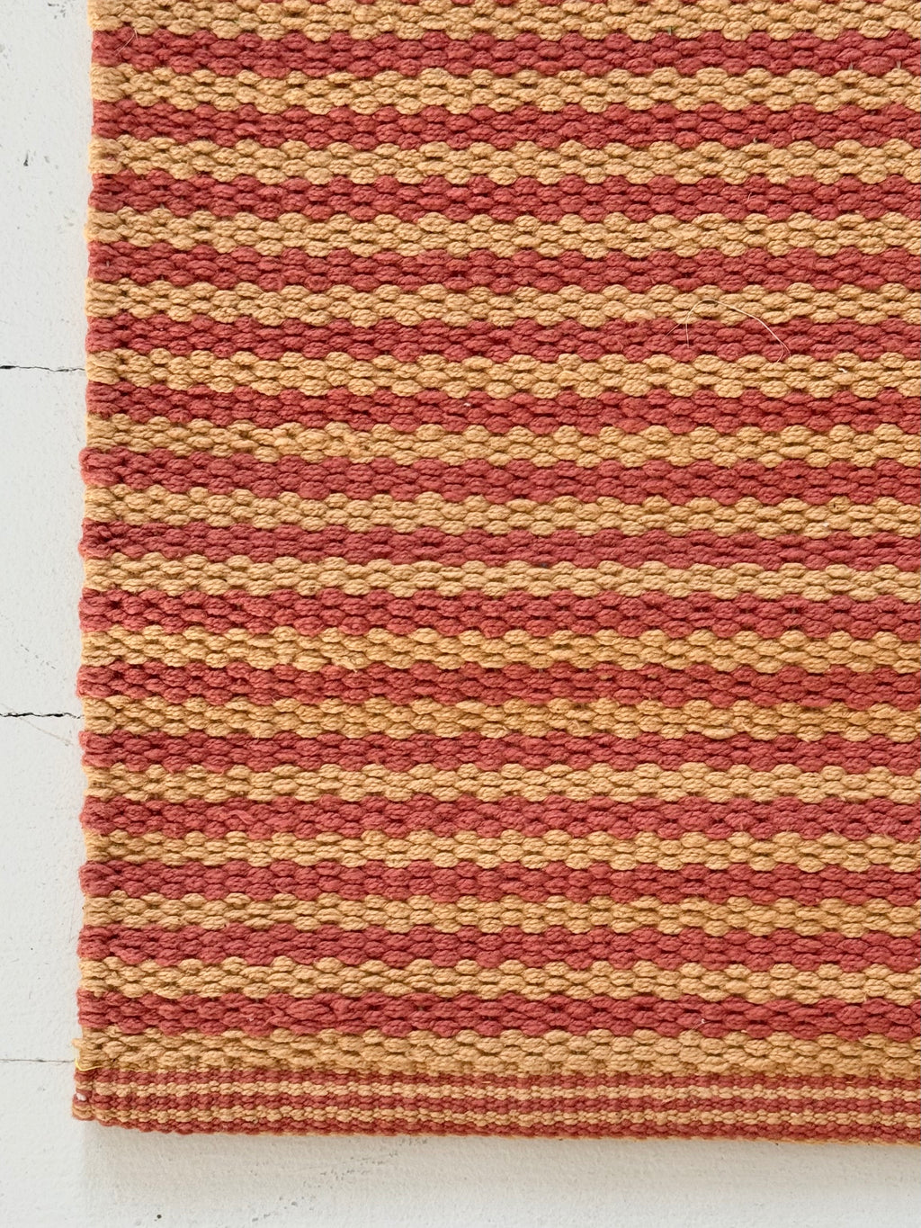 Striped red and beige rug on a white floor