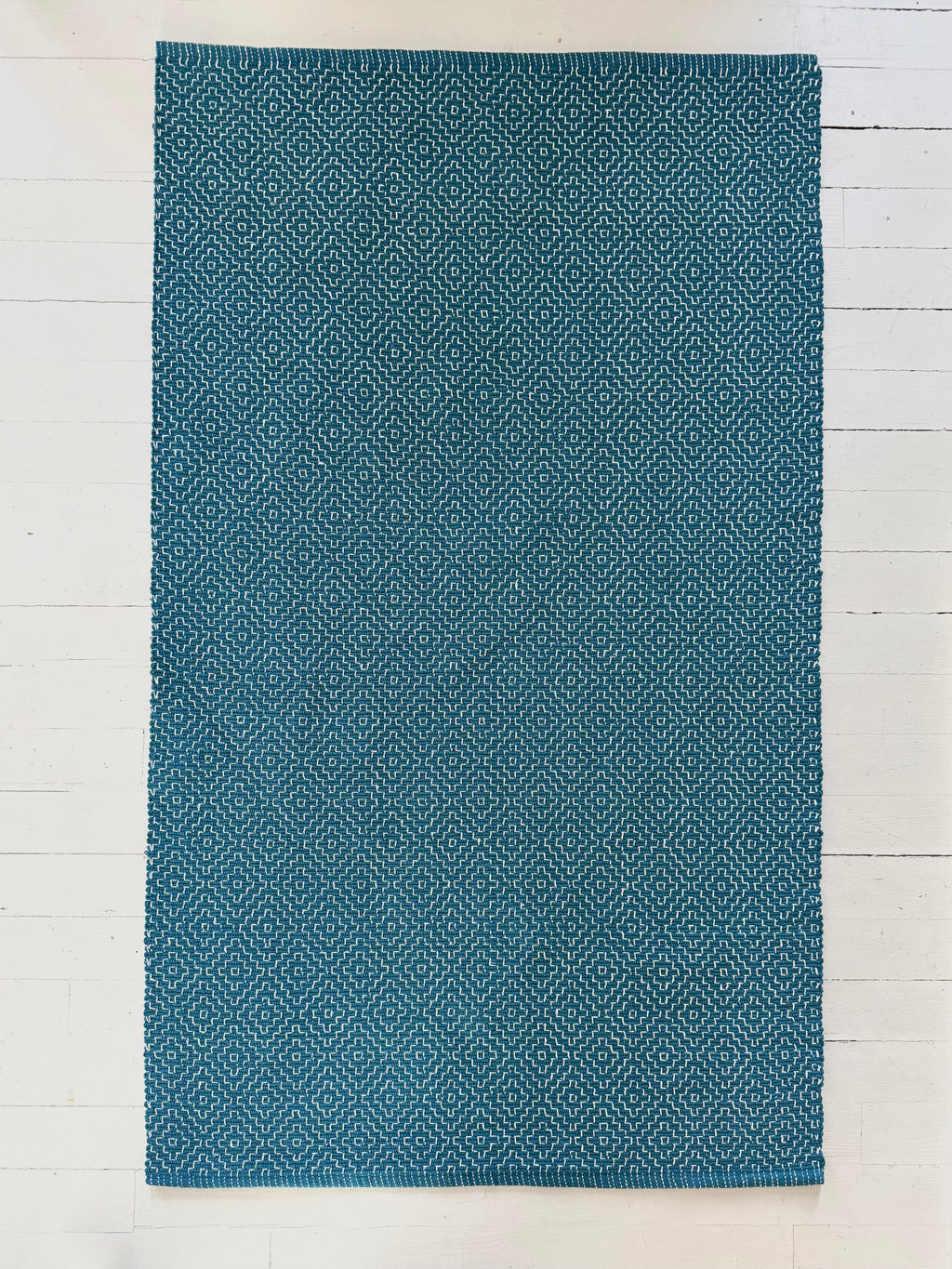Blue patterned cotton woven rug on a white wooden floor