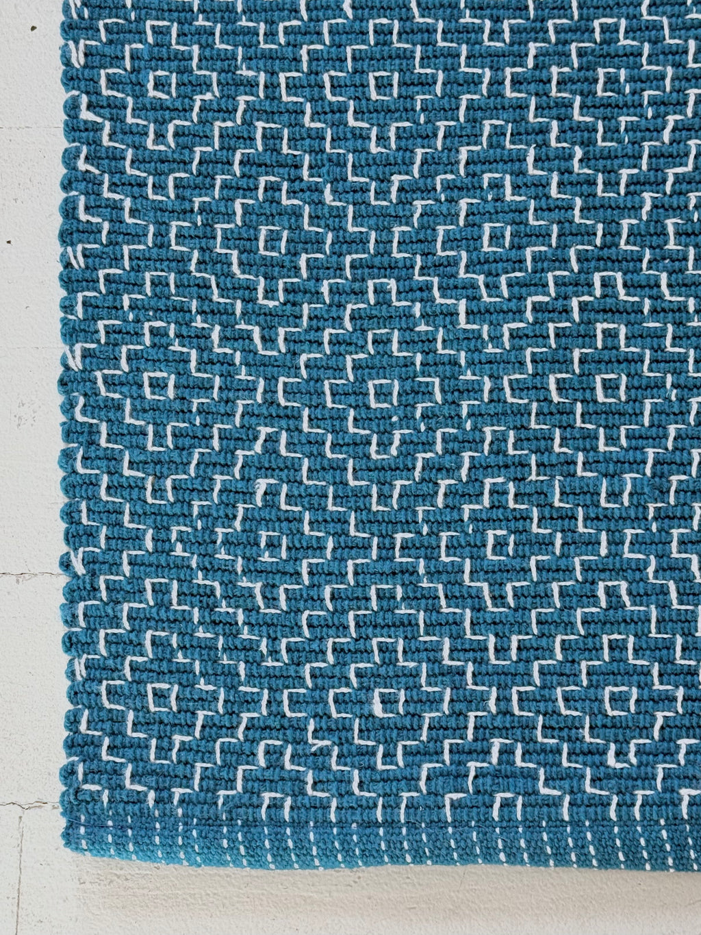 Blue textured cotton rug with geometric pattern on a light wood floor