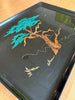 Decorative tray with tree designs in green, orange, and gold on a black background