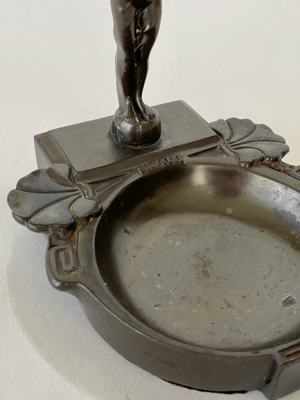 Bronze or similar metal sculpture of a figure on a pedestal with a circular base.