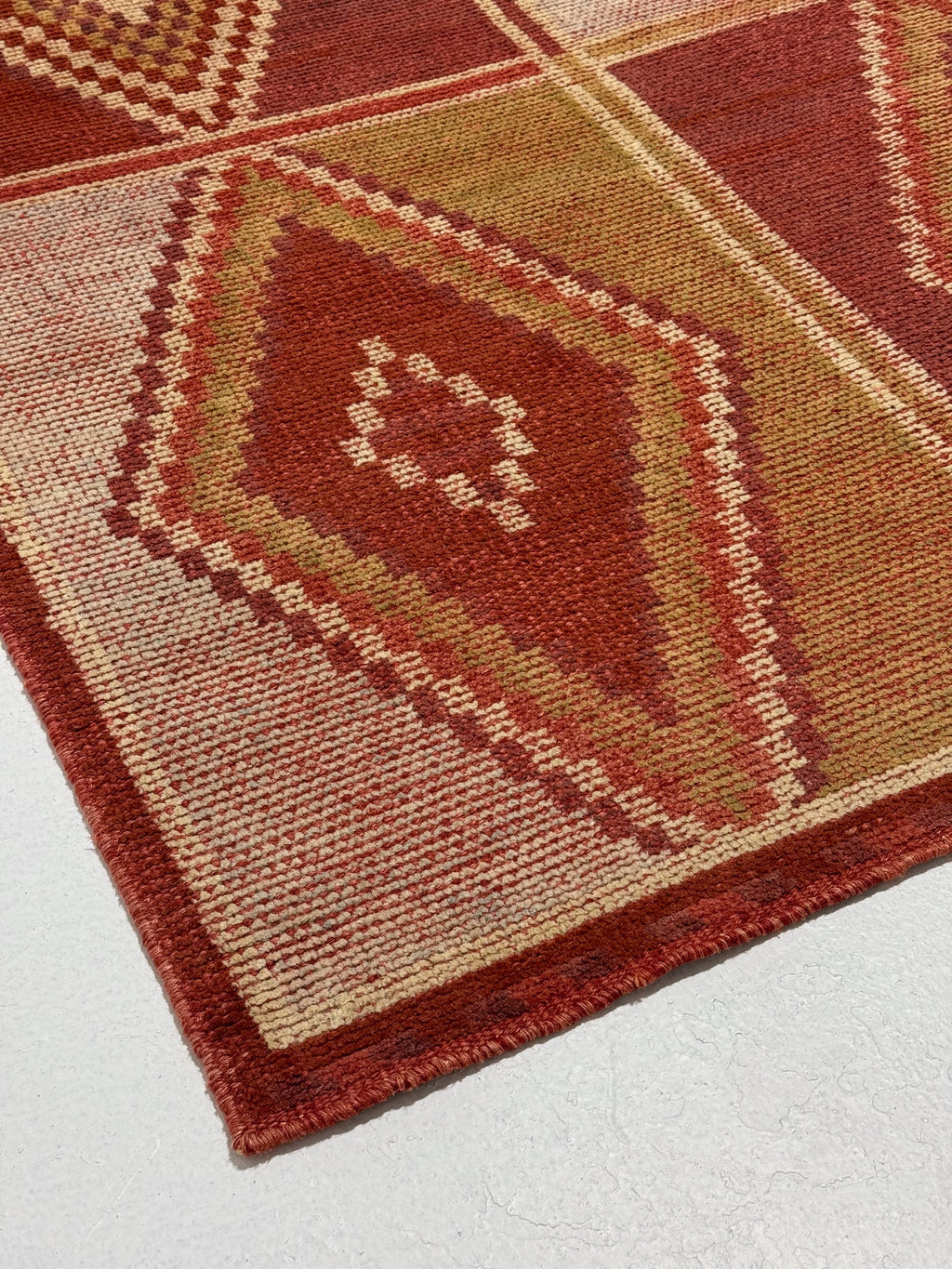 Close-up of a patterned red and beige rug on a light gray background