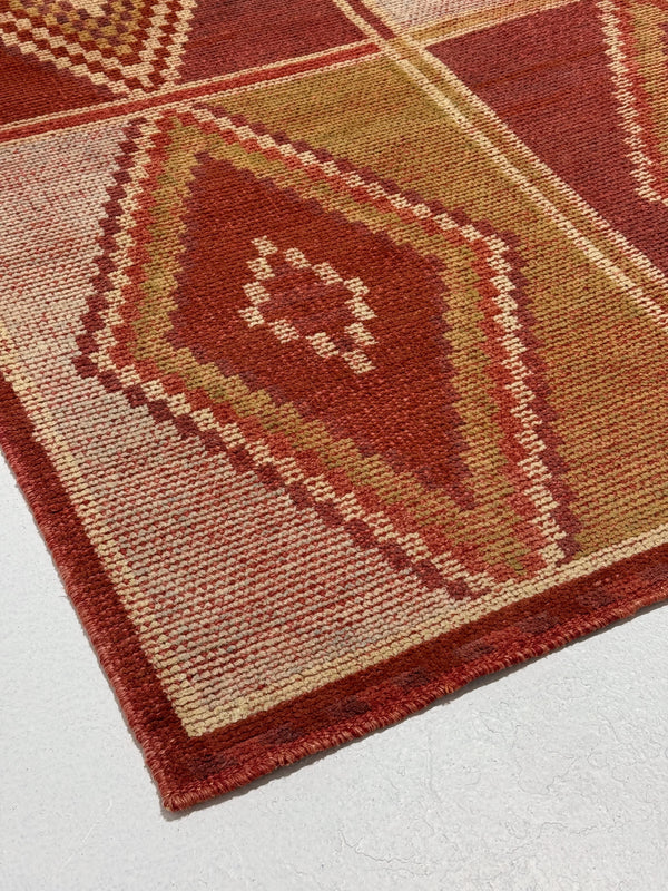 Close-up of a patterned red and beige rug on a light gray background