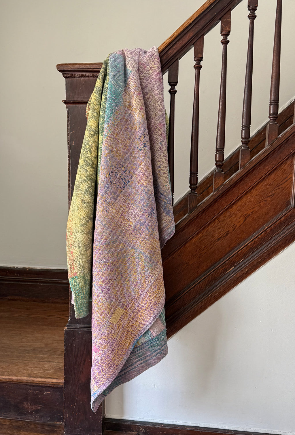 Colorful quilt draped over a wooden staircase rail.