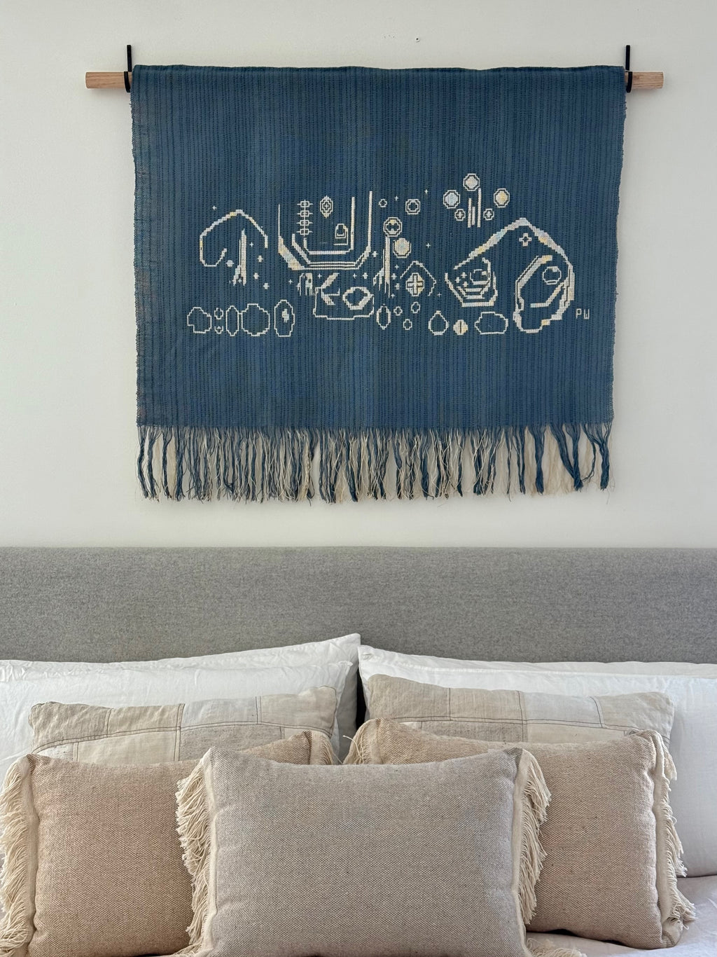 Blue woven tapestry with white patterns hanging above a sofa with beige pillows.