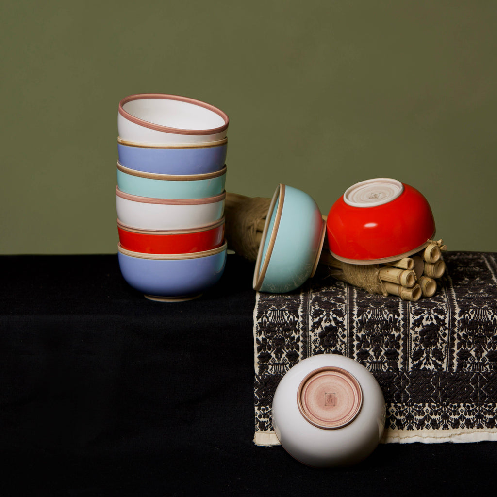 Colorful ceramic cups and bowls on a textured surface with a green background