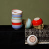 Colorful ceramic cups and bowls on a textured surface with a green background