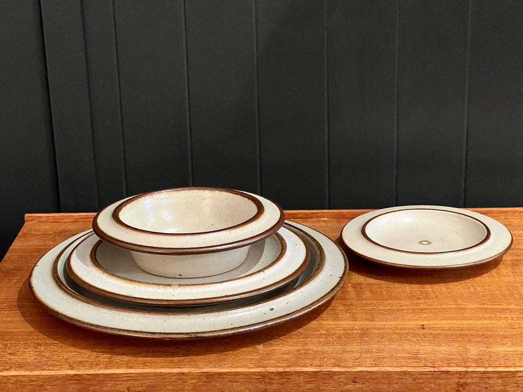 Set of ceramic plates with brown rim on a wooden surface against a dark paneled wall.