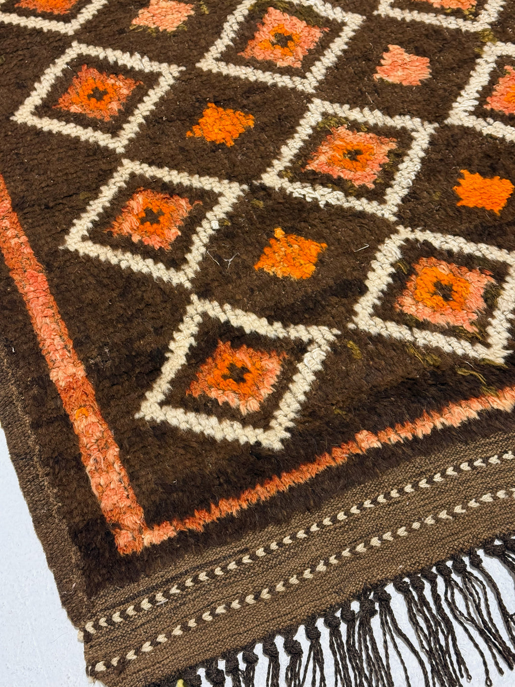 Close-up of a patterned rug with brown, orange, and white colors.