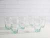 Set of six clear glasses on a white surface with a white tiled wall background