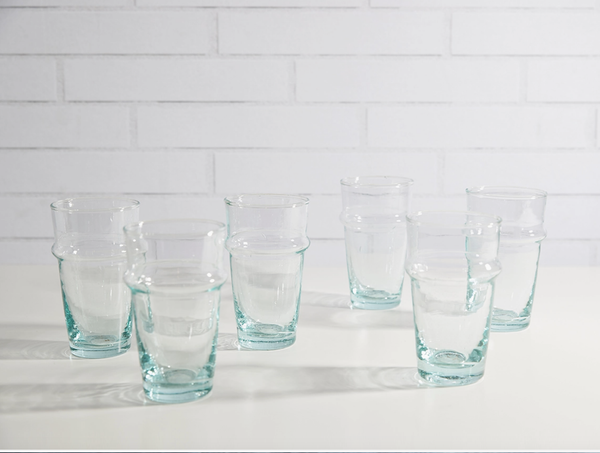 Set of six clear glasses on a white surface with a white tiled wall background