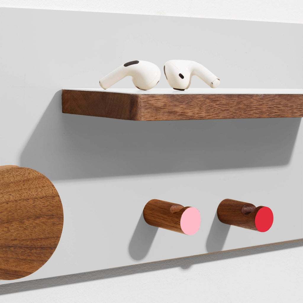 Wooden shelf with a wooden round hook, two wooden cylindrical hooks with pink and red ends, and a white object on a light gray background.