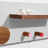 Wooden shelf with a wooden round hook, two wooden cylindrical hooks with pink and red ends, and a white object on a light gray background.