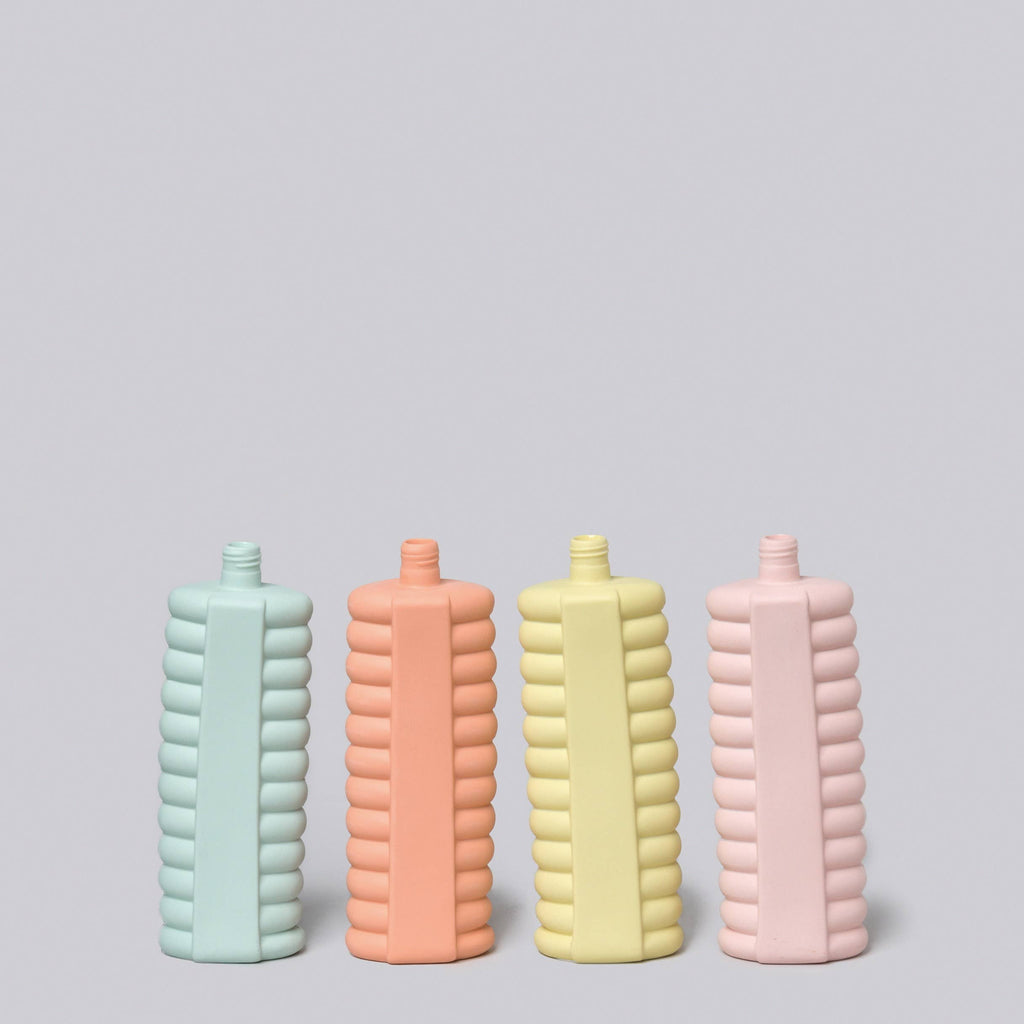 Four ribbed ceramic bottles in pastel colors on a light gray background