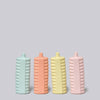 Four ribbed ceramic bottles in pastel colors on a light gray background