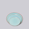 Set of three turquoise plates with natural clay rims on a light gray background