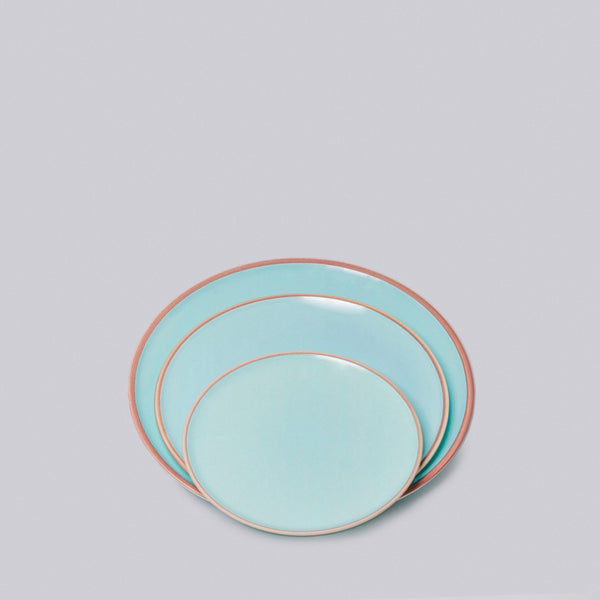 Set of three turquoise plates with natural clay rims on a light gray background