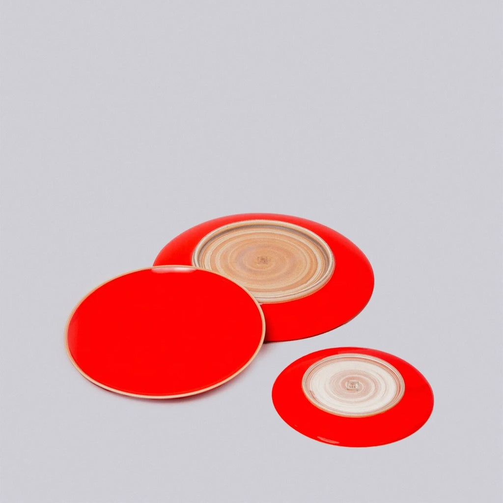 Three red circular plates with beige natural clay centers on a gray background