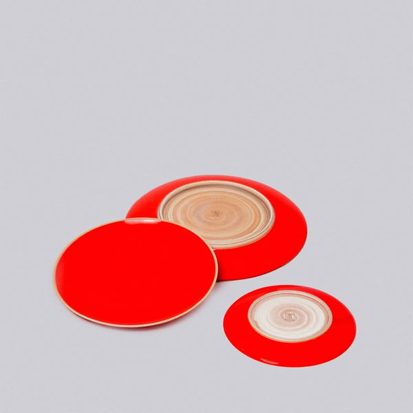 Three red circular plates with beige natural clay centers on a gray background