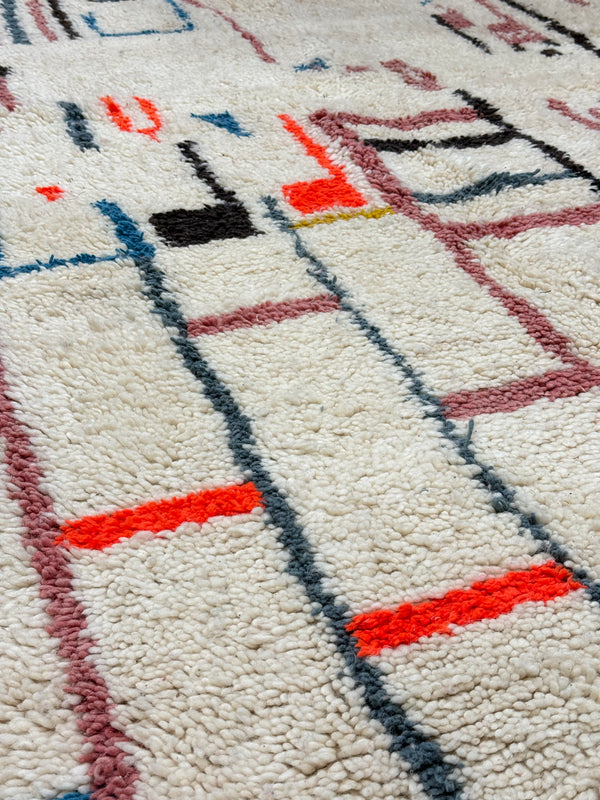 Close-up of a textured moroccan rug with geometric pattern in red, blue, and black on a beige background. high ply handwoven