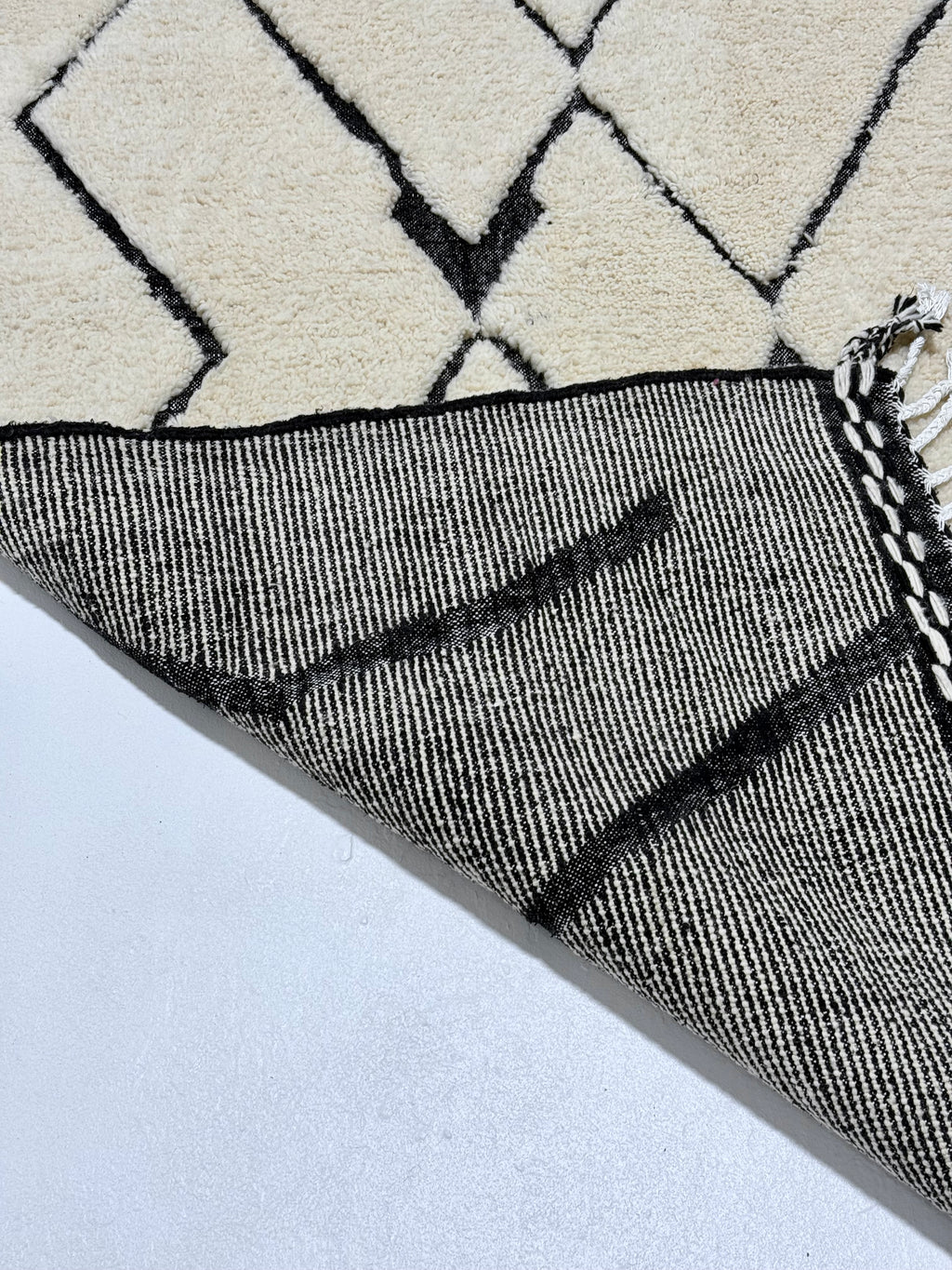 Close-up of a textured black and white rug with geometric pattern on a light gray background