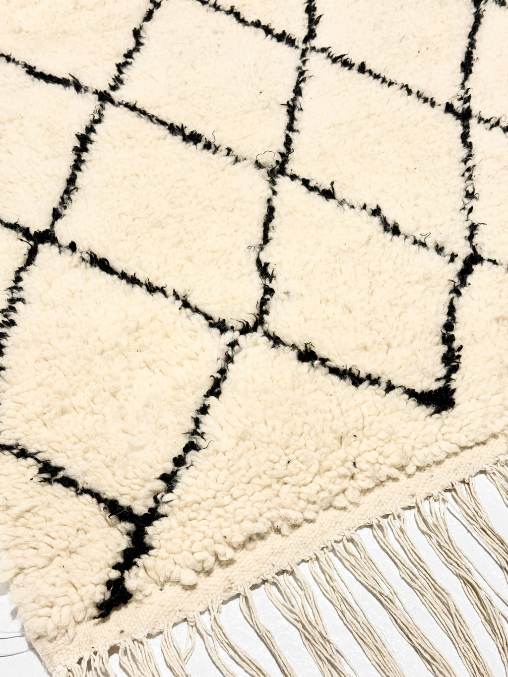 Close-up of a white rug with black geometric pattern and fringes