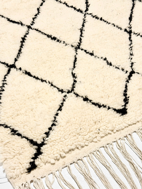 Close-up of a white rug with black geometric pattern and fringes