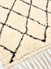 Close-up of a white rug with black geometric pattern and fringes