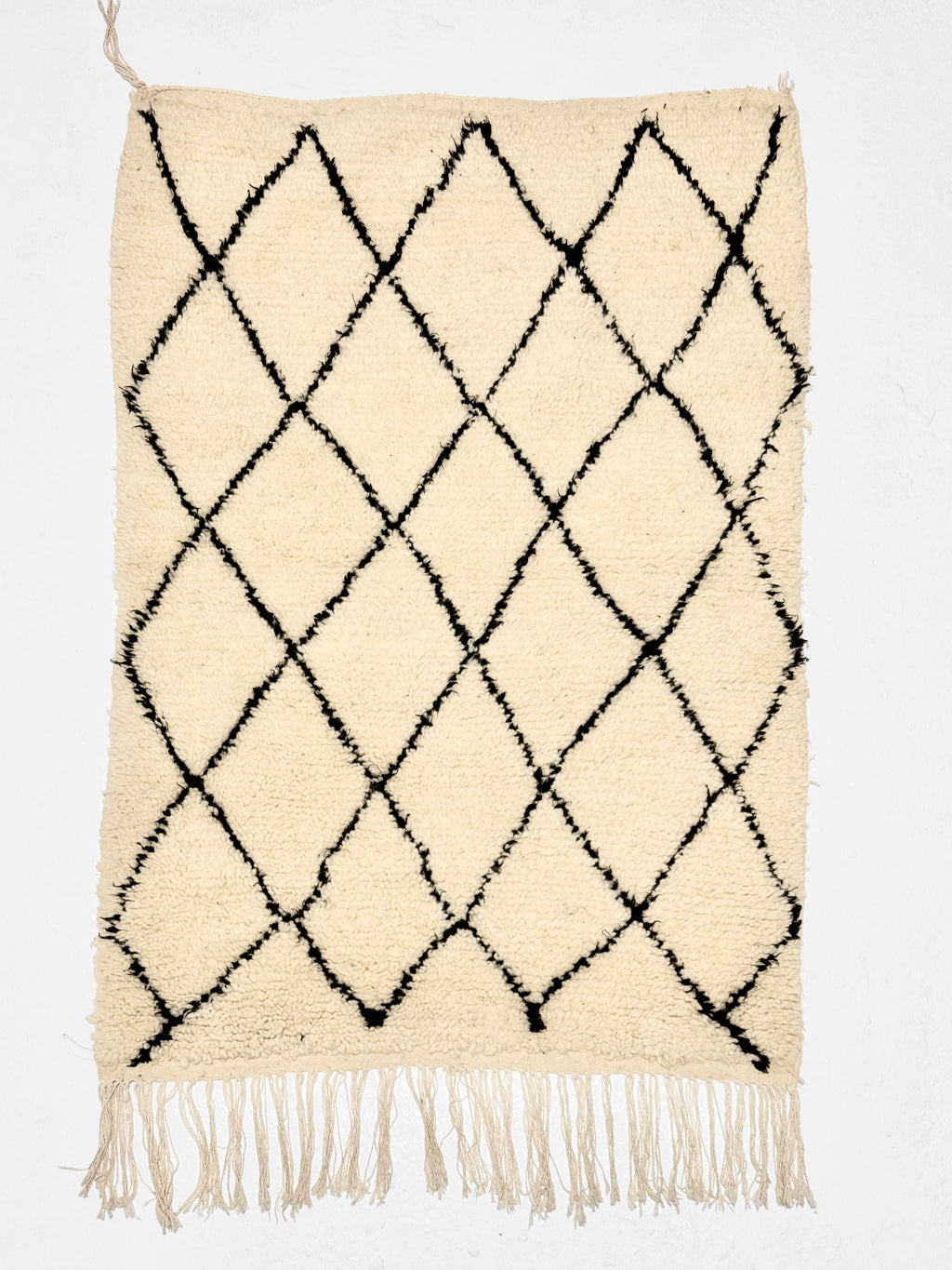 Beige rug with black diamond pattern and white fringe on a white background