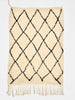 Beige rug with black diamond pattern and white fringe on a white background