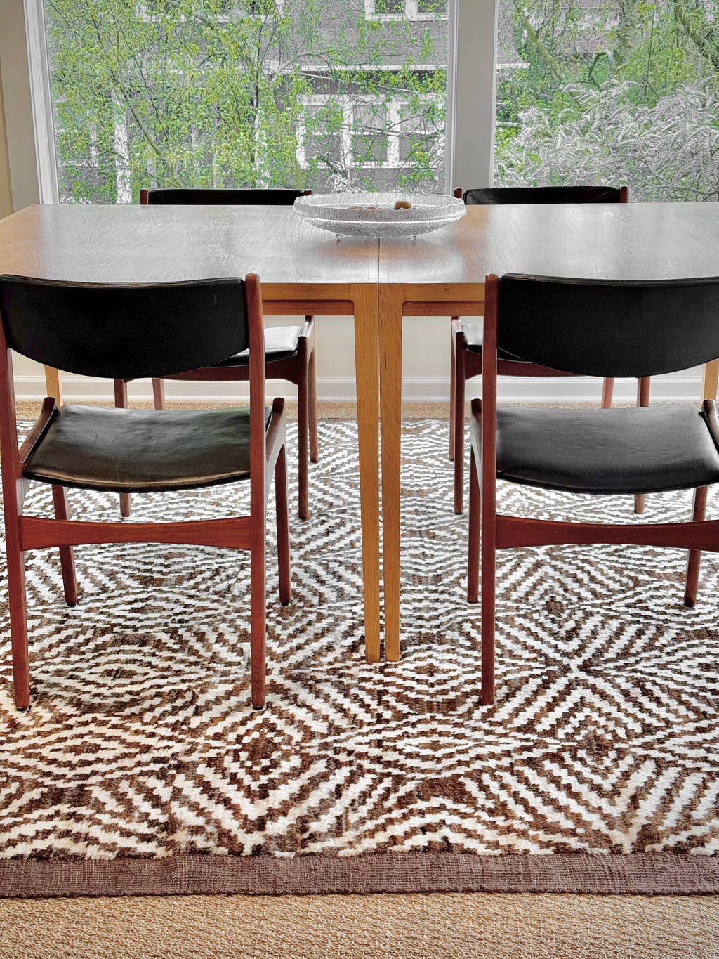 Dining room with a wooden table and black chairs on a patterned rug.