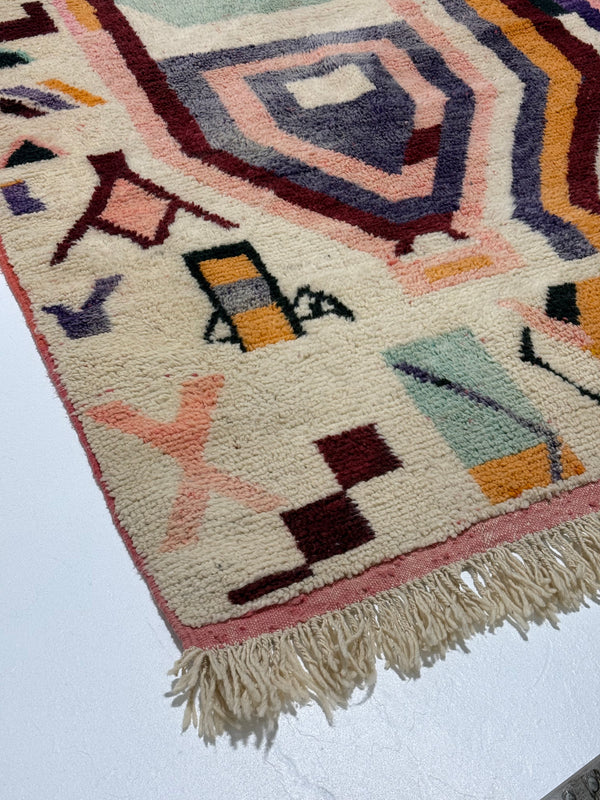 Close-up of a colorful geometric-patterned rug with fringes on a white background