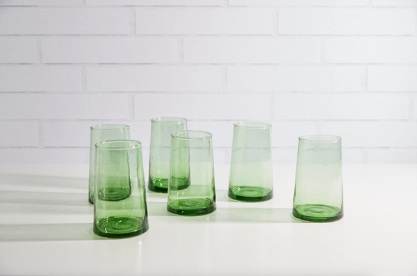Set of green glass tumblers on a white surface with a tiled wall background