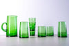Set of green glass tumblers on a light gray surface with a white background