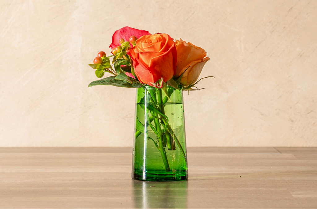 Green glass vase with colorful flowers on a wooden surface